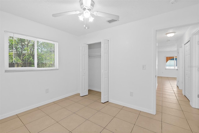 unfurnished bedroom featuring multiple windows, ceiling fan, a closet, and light tile patterned flooring