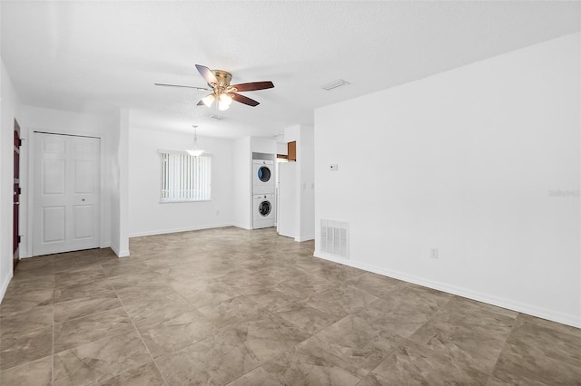 unfurnished living room featuring ceiling fan and stacked washing maching and dryer