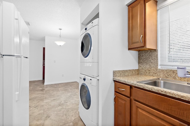 clothes washing area with a textured ceiling, sink, and stacked washer / dryer