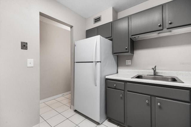 kitchen with light tile patterned floors, white refrigerator, gray cabinetry, and sink