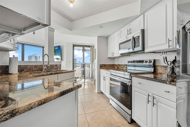 kitchen featuring appliances with stainless steel finishes, dark stone counters, sink, white cabinets, and light tile patterned flooring