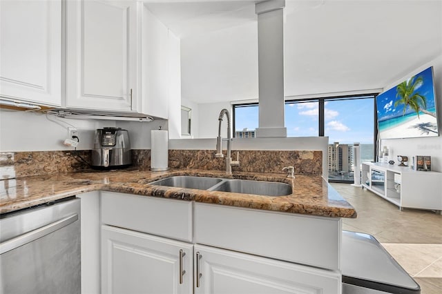 kitchen featuring stainless steel dishwasher, sink, a wall of windows, dark stone countertops, and white cabinetry