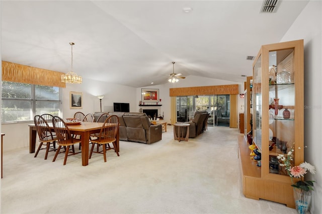 dining space with ceiling fan with notable chandelier, a healthy amount of sunlight, light carpet, and vaulted ceiling