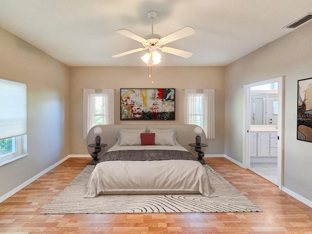 bedroom with ensuite bathroom, ceiling fan, light hardwood / wood-style flooring, and multiple windows