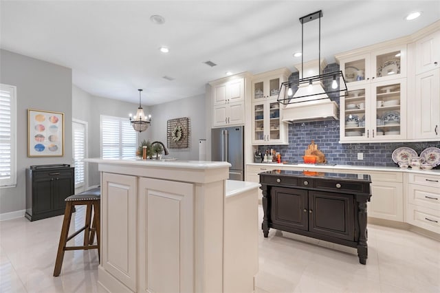 kitchen with an island with sink, decorative light fixtures, high quality fridge, decorative backsplash, and a breakfast bar