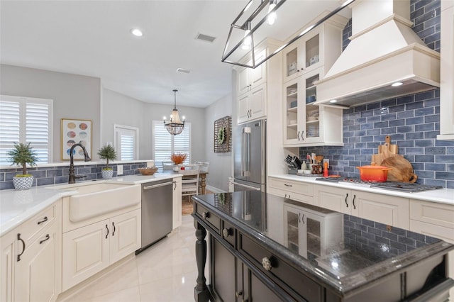 kitchen with pendant lighting, dark stone counters, appliances with stainless steel finishes, tasteful backsplash, and custom range hood