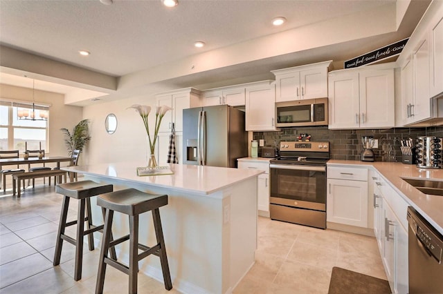 kitchen featuring appliances with stainless steel finishes, light tile patterned floors, white cabinetry, and a kitchen island