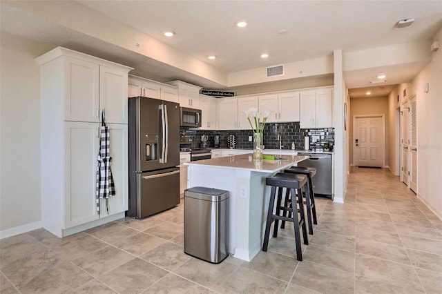 kitchen with appliances with stainless steel finishes, a kitchen breakfast bar, light tile patterned floors, a center island, and white cabinetry