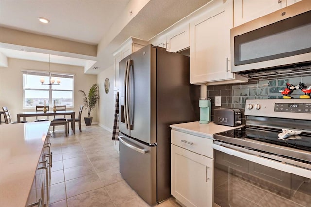 kitchen with appliances with stainless steel finishes, backsplash, white cabinets, a chandelier, and hanging light fixtures