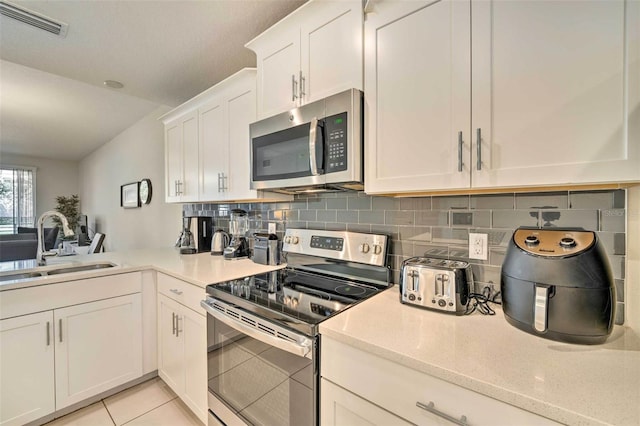 kitchen featuring decorative backsplash, appliances with stainless steel finishes, sink, light tile patterned floors, and white cabinets