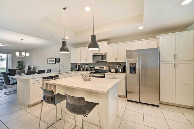 kitchen with kitchen peninsula, hanging light fixtures, appliances with stainless steel finishes, and a tray ceiling