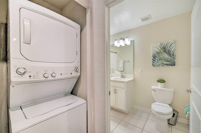 washroom featuring sink, light tile patterned floors, a textured ceiling, and stacked washer and clothes dryer