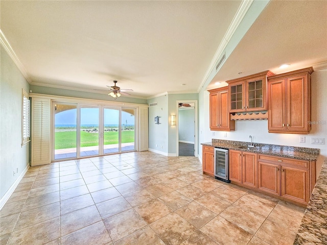 kitchen with ceiling fan, dark stone countertops, ornamental molding, light tile patterned flooring, and beverage cooler