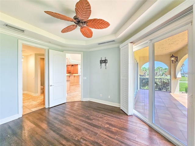 unfurnished room with a tray ceiling, ceiling fan, dark hardwood / wood-style floors, and ornamental molding