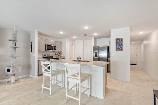 kitchen featuring a kitchen bar, stainless steel appliances, sink, a center island with sink, and gray cabinets