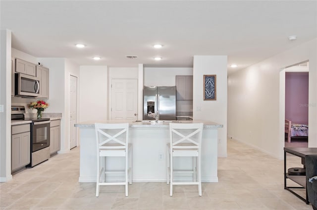 kitchen featuring gray cabinetry, stainless steel appliances, a kitchen island with sink, sink, and a breakfast bar area