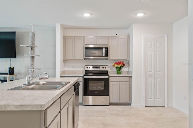 kitchen featuring gray cabinetry, sink, stainless steel appliances, and a center island with sink