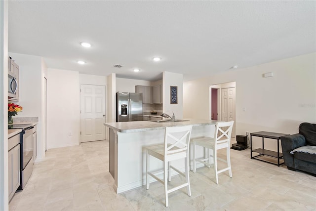 kitchen with sink, stainless steel appliances, a breakfast bar area, gray cabinets, and a kitchen island with sink