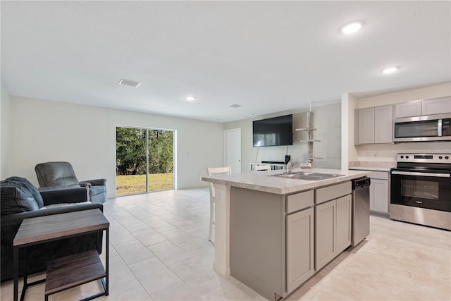 kitchen featuring gray cabinetry, sink, stainless steel appliances, an island with sink, and light tile patterned floors