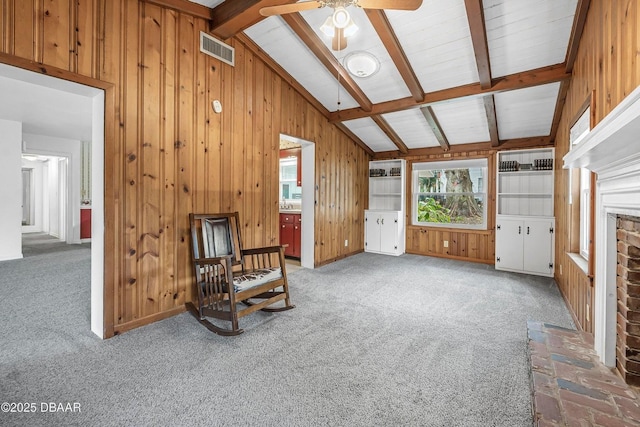 sitting room with carpet flooring, vaulted ceiling with beams, ceiling fan, and wooden walls