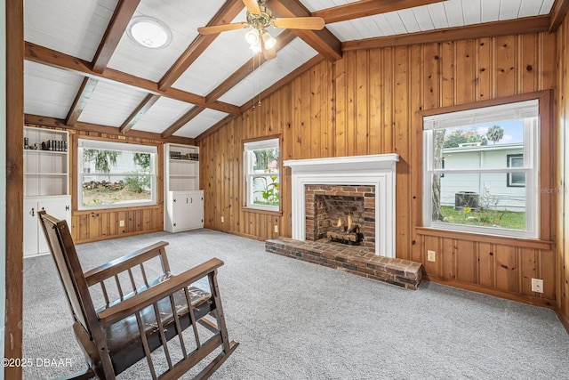 carpeted living room featuring lofted ceiling with beams, ceiling fan, a fireplace, and wooden walls