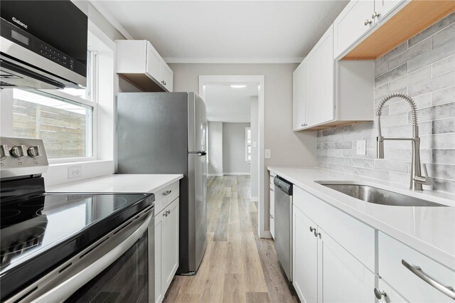 kitchen with decorative backsplash, appliances with stainless steel finishes, sink, white cabinets, and light hardwood / wood-style floors