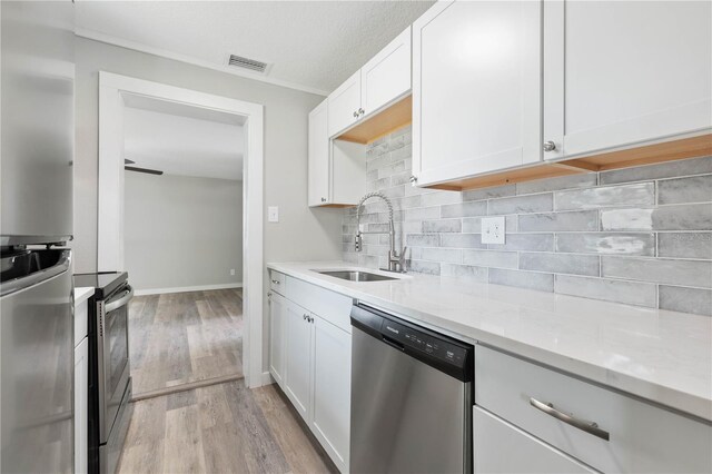 kitchen with white cabinets, sink, appliances with stainless steel finishes, light hardwood / wood-style floors, and light stone counters