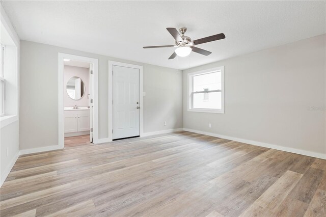 unfurnished bedroom with light wood-type flooring, connected bathroom, ceiling fan, and sink