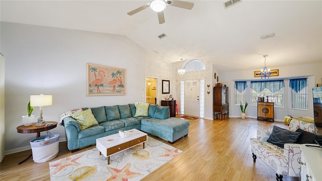 living room with ceiling fan with notable chandelier, light hardwood / wood-style floors, and vaulted ceiling