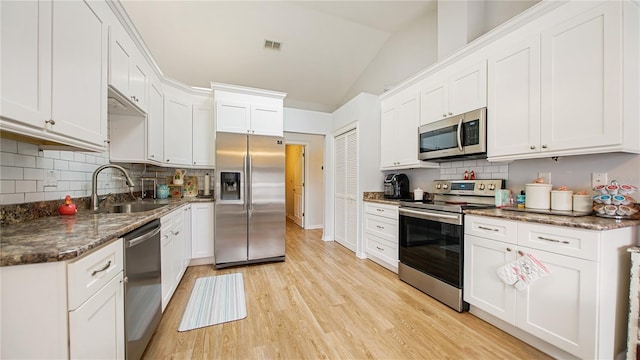 kitchen featuring dark stone counters, stainless steel appliances, sink, white cabinets, and lofted ceiling