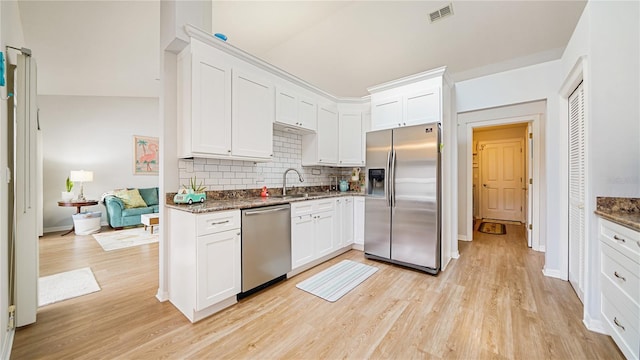 kitchen with dark stone counters, white cabinets, sink, light wood-type flooring, and stainless steel appliances