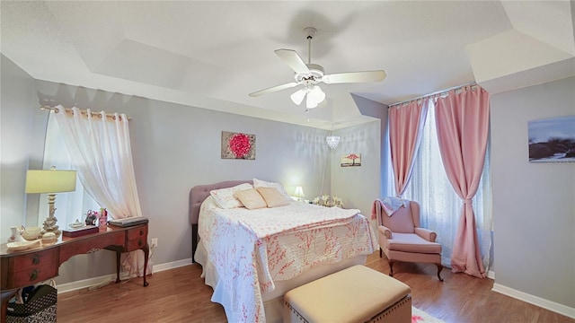 bedroom with hardwood / wood-style flooring, ceiling fan, and a raised ceiling