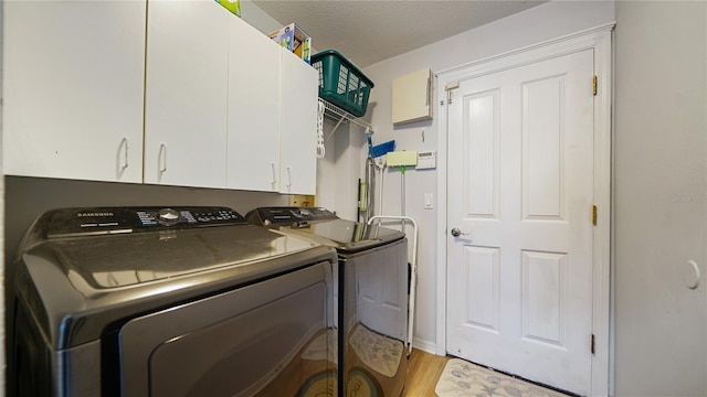 laundry room with cabinets, independent washer and dryer, a textured ceiling, and light wood-type flooring