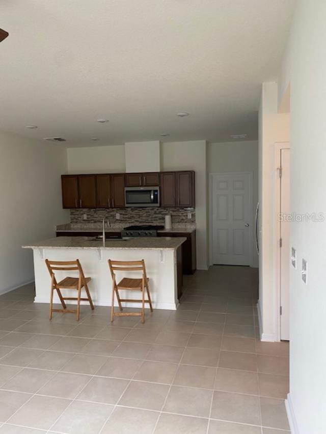 kitchen featuring sink, a kitchen breakfast bar, backsplash, a kitchen island with sink, and light tile patterned floors