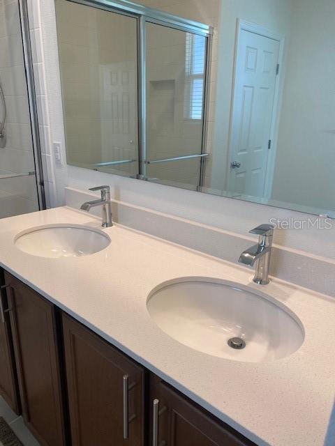 full bath featuring double vanity, a sink, and tiled shower