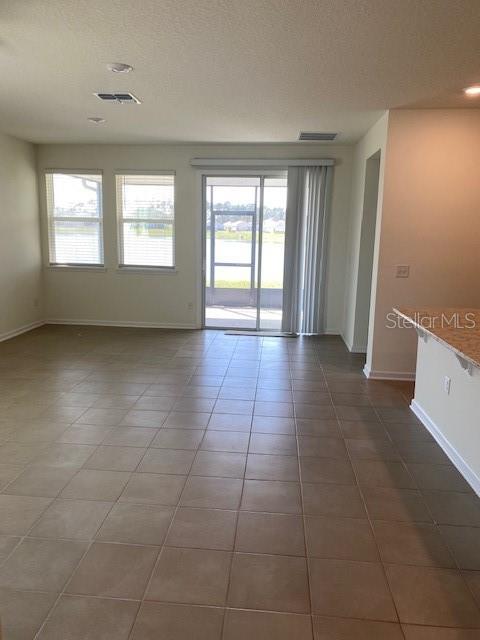 spare room with baseboards, visible vents, a textured ceiling, and dark tile patterned flooring