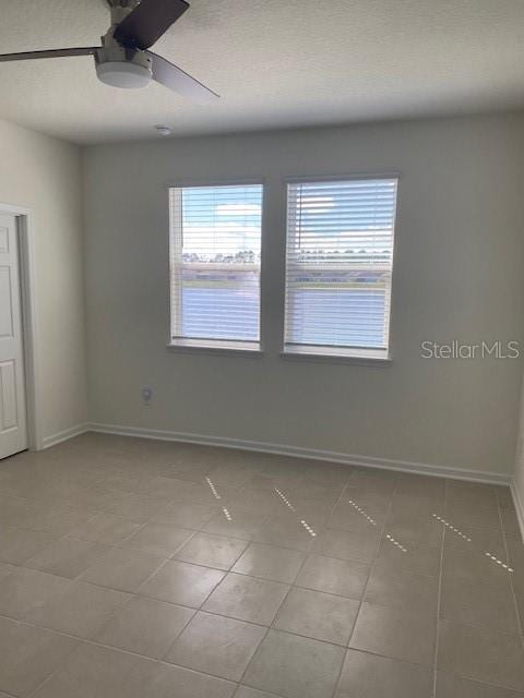 unfurnished room with light tile patterned floors, plenty of natural light, baseboards, and a ceiling fan