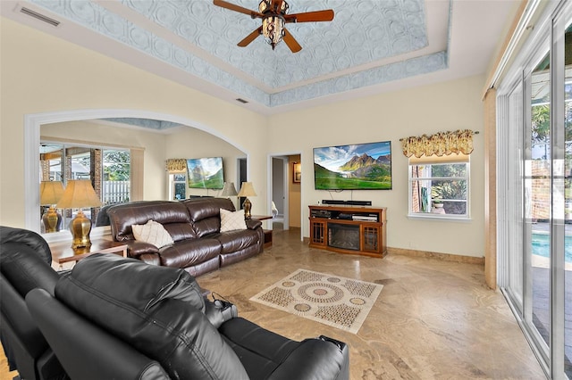 living room featuring ceiling fan, a high ceiling, and a tray ceiling