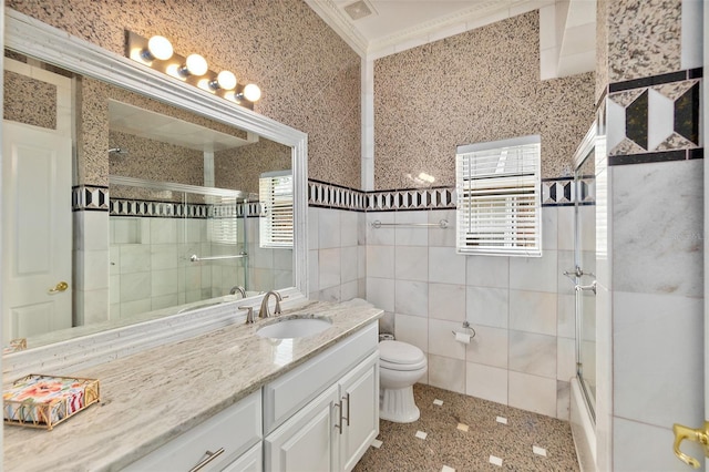 full bathroom with combined bath / shower with glass door, toilet, vanity, tile walls, and ornamental molding