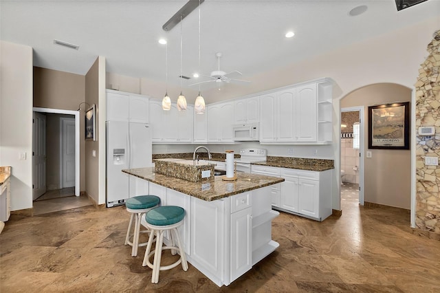 kitchen with white cabinets, dark stone countertops, white appliances, and an island with sink