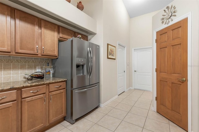 kitchen featuring stone countertops, light tile patterned flooring, decorative backsplash, and stainless steel refrigerator with ice dispenser