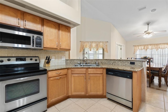 kitchen featuring sink, stainless steel appliances, light stone counters, kitchen peninsula, and vaulted ceiling