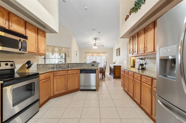 kitchen with light stone countertops, stainless steel appliances, ceiling fan, sink, and lofted ceiling