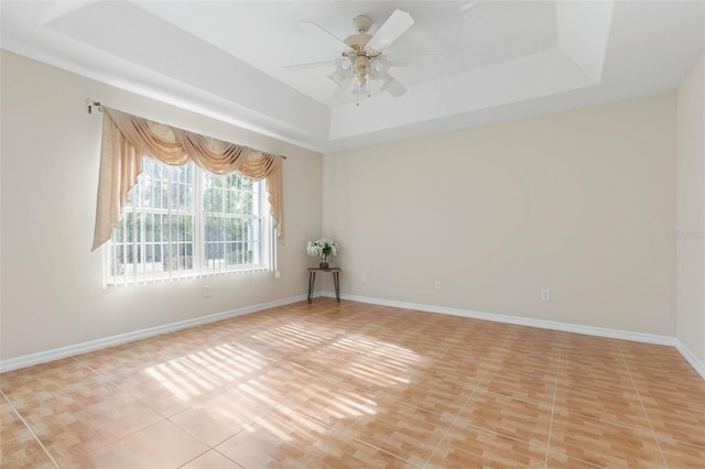 spare room featuring a raised ceiling, ceiling fan, and light tile patterned floors