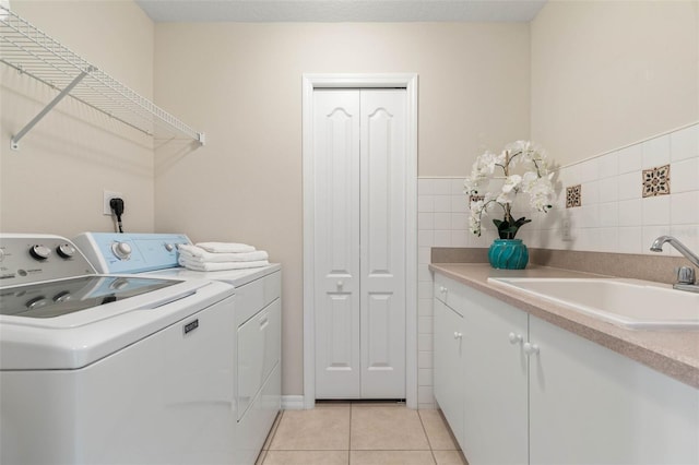 laundry room featuring washing machine and clothes dryer, sink, light tile patterned flooring, and cabinets