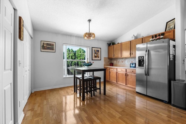 kitchen with backsplash, stainless steel fridge, light hardwood / wood-style flooring, and decorative light fixtures