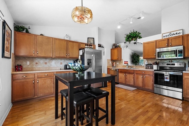 kitchen featuring appliances with stainless steel finishes, backsplash, vaulted ceiling, pendant lighting, and light hardwood / wood-style floors