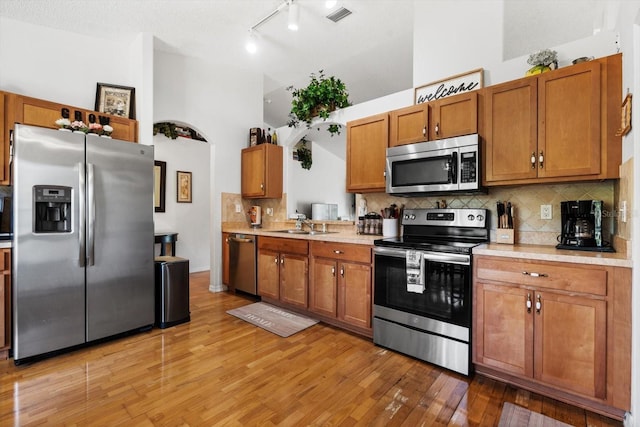 kitchen featuring sink, a high ceiling, light hardwood / wood-style floors, decorative backsplash, and appliances with stainless steel finishes