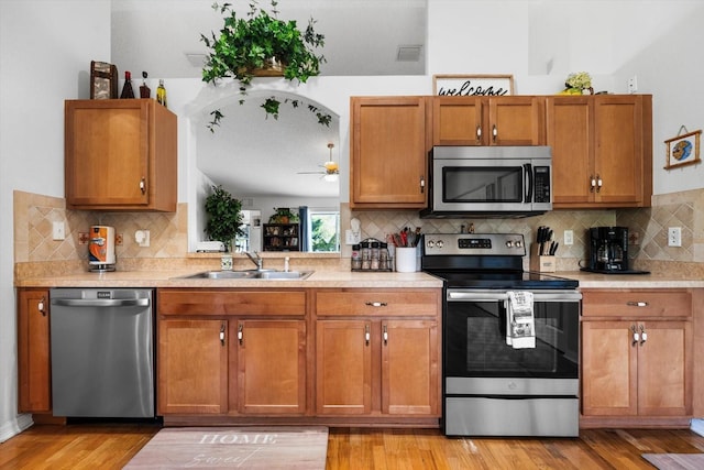 kitchen featuring decorative backsplash, appliances with stainless steel finishes, light wood-type flooring, ceiling fan, and sink