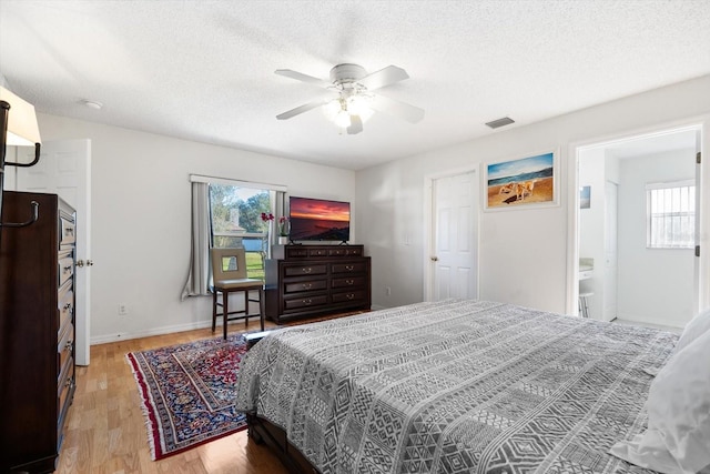 bedroom with ceiling fan, ensuite bathroom, wood-type flooring, and a textured ceiling